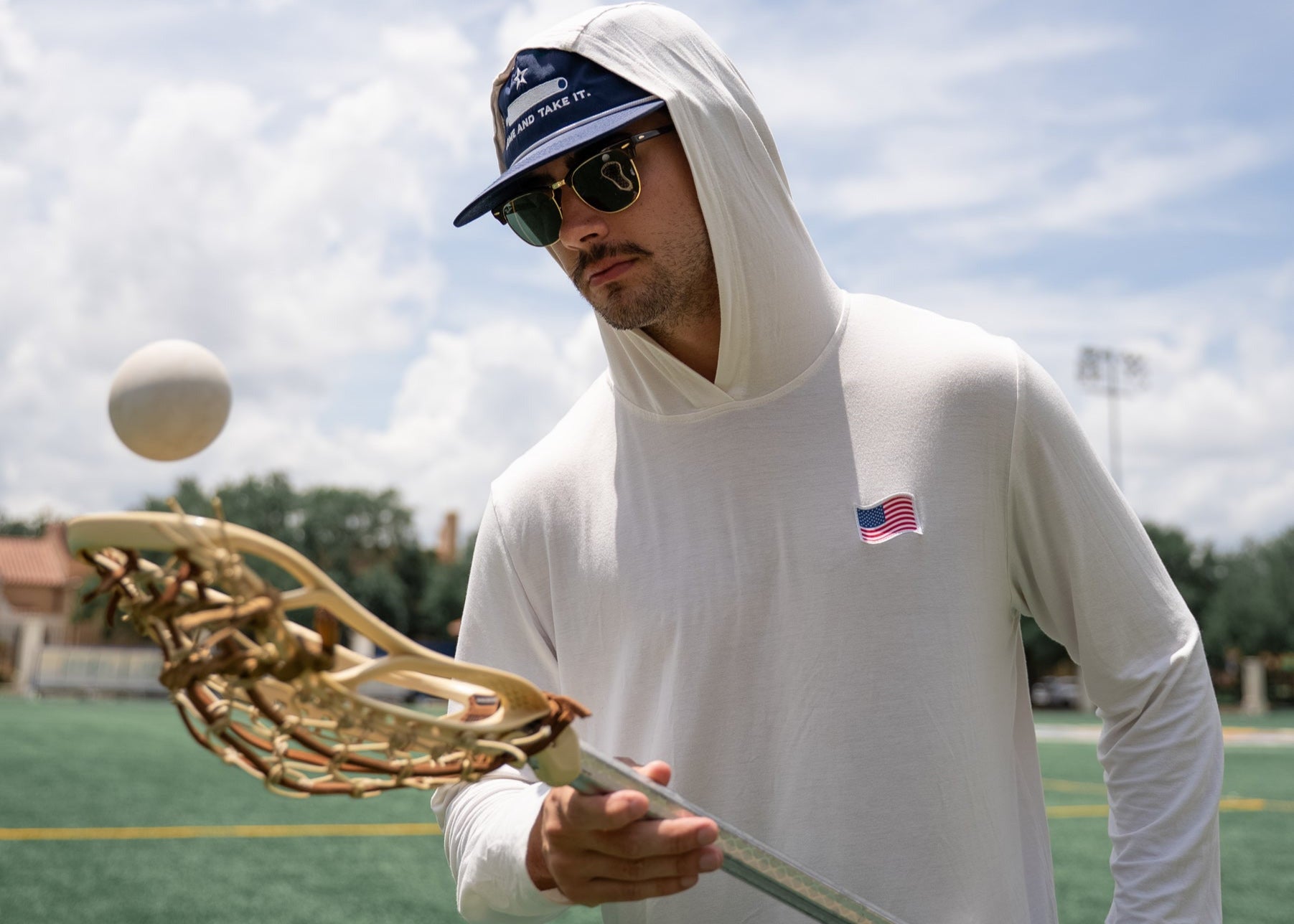 Man holding a lacrosse stick on a sports field with a blue sky.